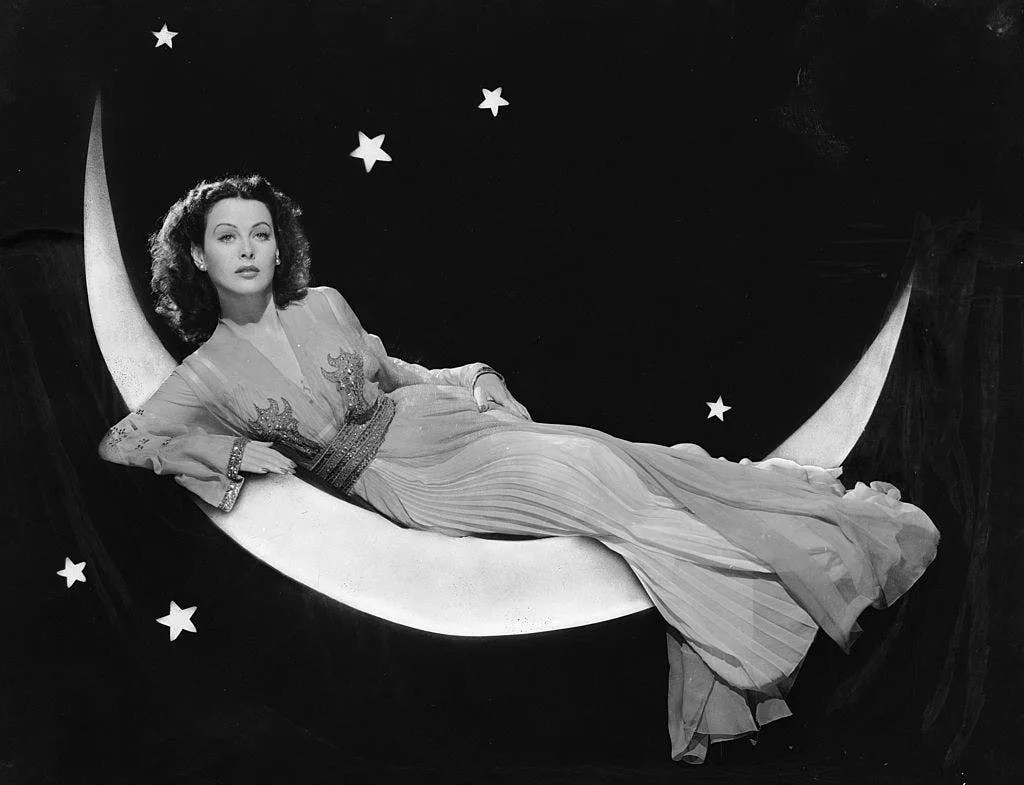 August 4, 1943: Austrian-born actress Hedy Lamarr (1913-2000) models a long flowing dress while reclining on a crescent moon in a publicity shot for her film "The Heavenly Body."