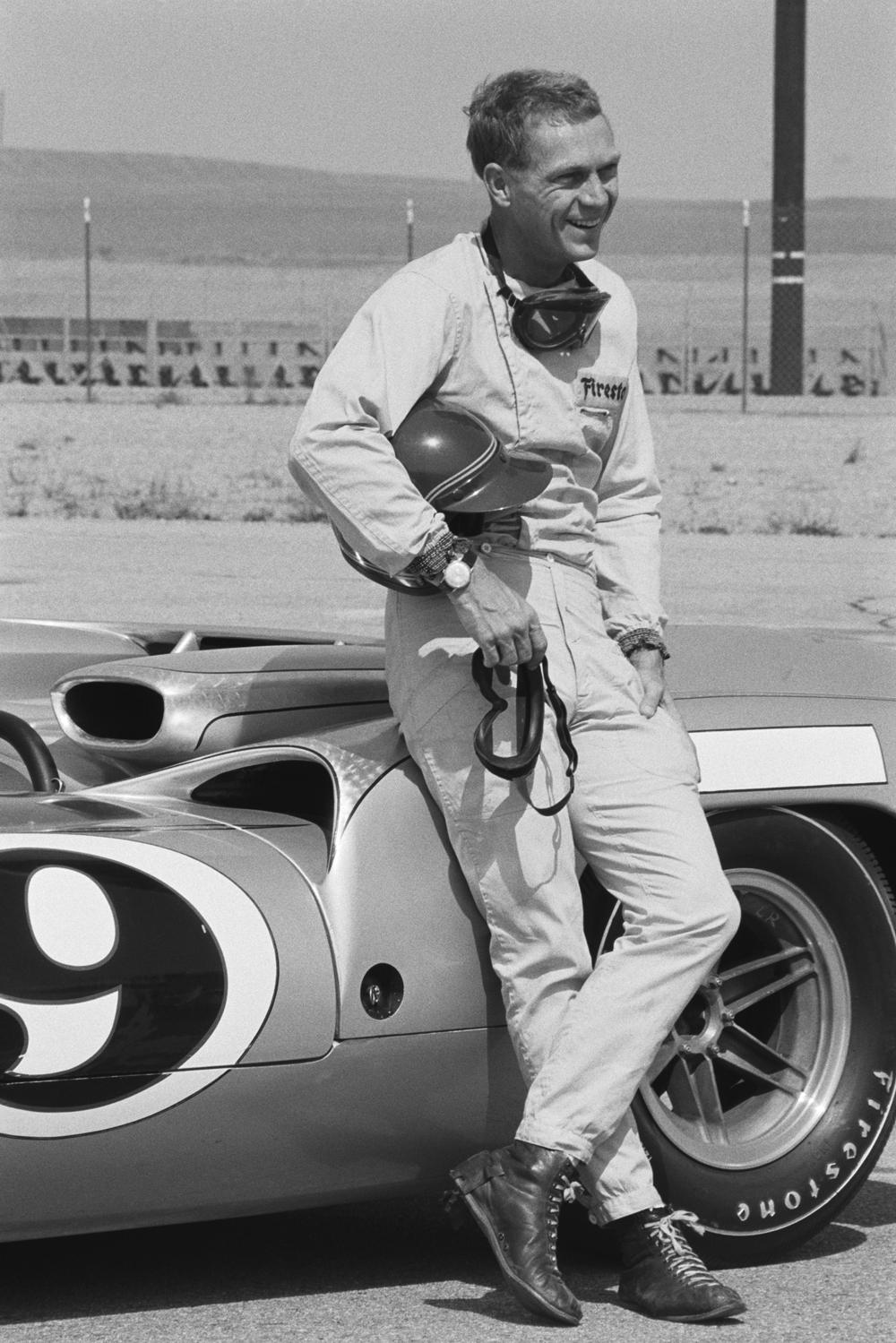 Steve McQueen in racing attire leaning against a race car