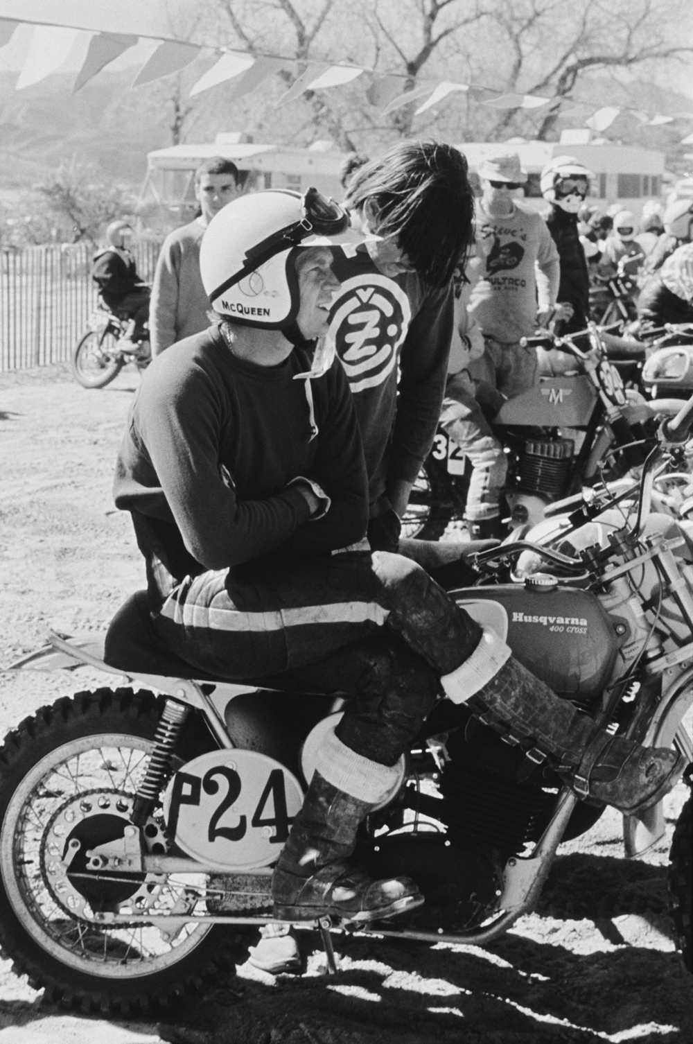Steve McQueen in racing attire sitting on motorcycle