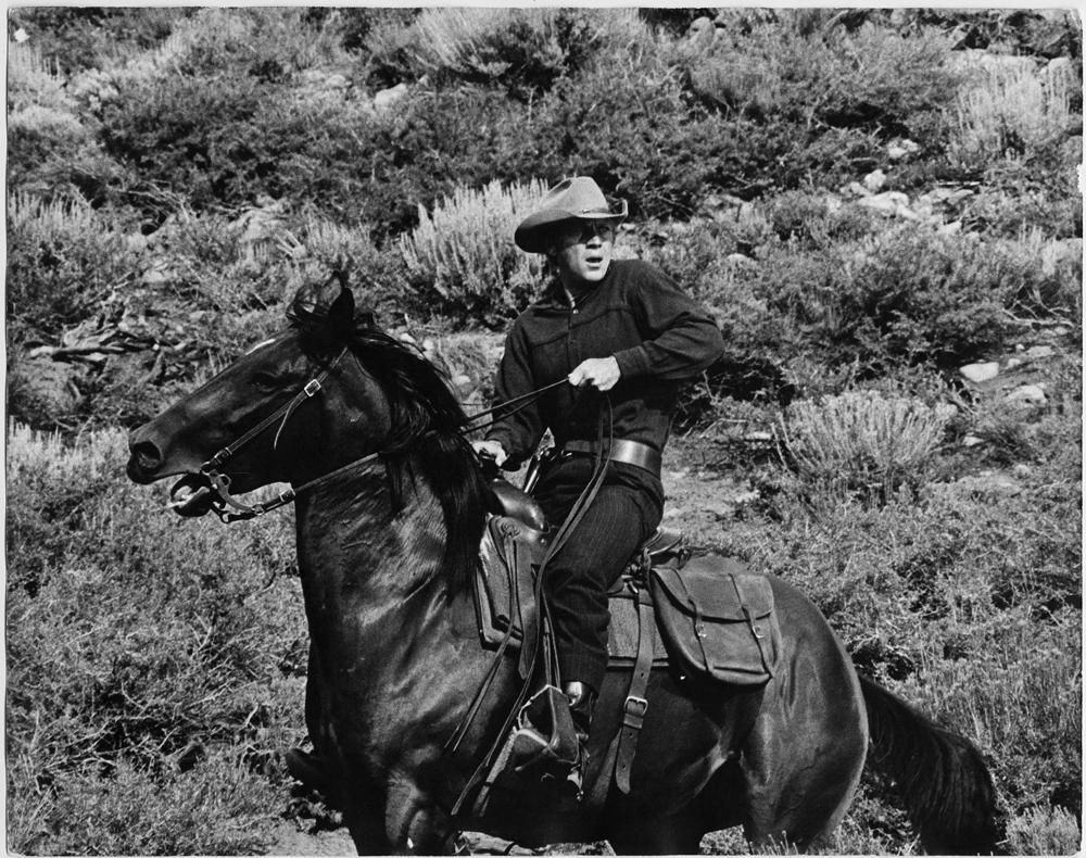 Steve McQueen wearing a cowboy hat while on a horse